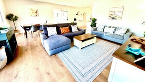 A modern living room with a grey sectional sofa, a coffee table, and a dining area with a table and chairs.