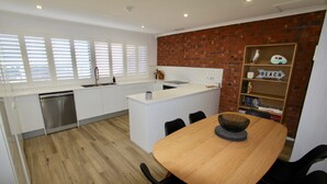 Una cocina moderna con armarios blancos, una pared de acento de ladrillo y un comedor con una mesa y sillas de madera.