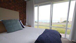 Habitación de hotel con una cama grande, una pared de ladrillo y vistas al mar a través de amplios ventanales.