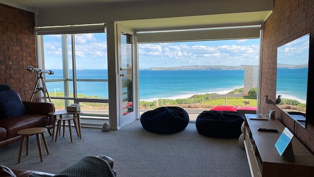 Una habitación con un amplio ventanal que ofrece vistas al océano, un telescopio y una zona de estar acogedora con sofá y sillones.
