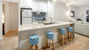 Une cuisine moderne avec des meubles blancs, un réfrigérateur encastré, un évier et des tabourets de bar dotés de coussins à motifs.