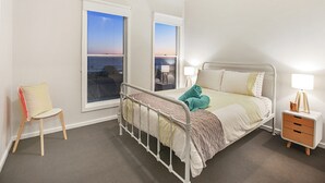 Une chambre à coucher comprenant un lit, des tables de chevet, une chaise et de grandes fenêtres donnant sur un beau paysage.
