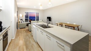 Une cuisine moderne dotée d’un îlot central, d’un coin repas avec une table et des chaises en bois, et offrant une vue sur la mer grâce à une grande fenêtre.