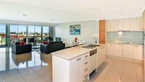 A modern kitchen with white cabinets, a central island, and a dining area with a sofa and chairs. - 3BR Penthouse w/ Ocean Views – Pool, Spa Bath, Tennis Court & Secured Parking | Ideal for Extended Stays (Victor Harbor)
