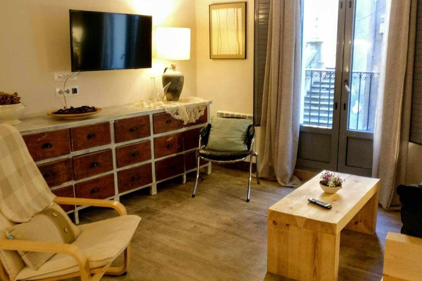 Een woonkamer met een houten kast, een televisie, een stoel, een tafel en een raam met gordijnen.