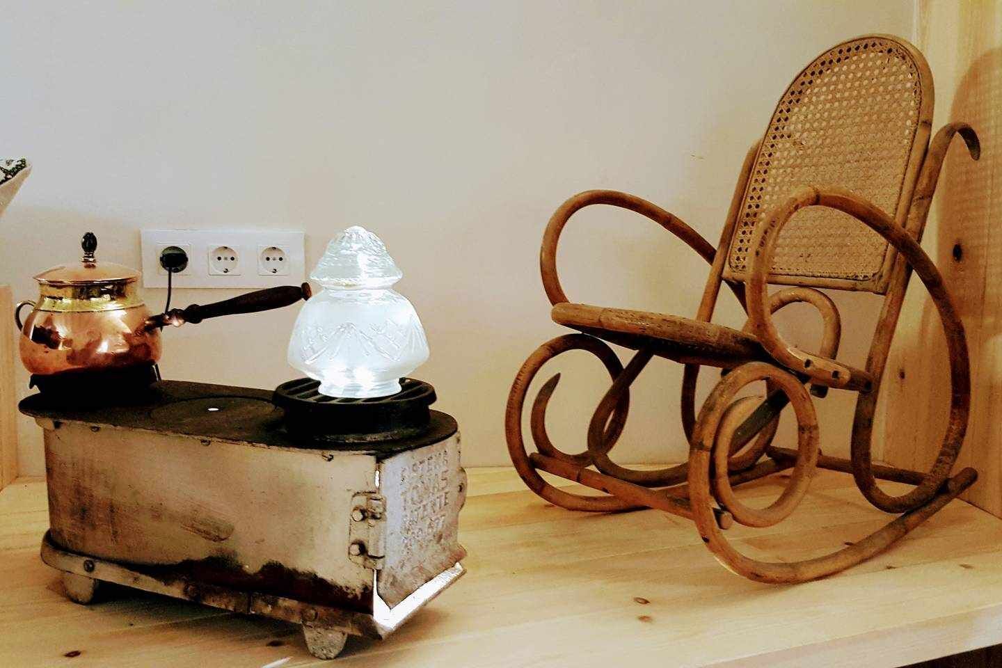 Une cuisine au style rustique, avec un poêle ancien, une bouilloire électrique à surface vitrocéramique et un fauteuil à bascule en bois.