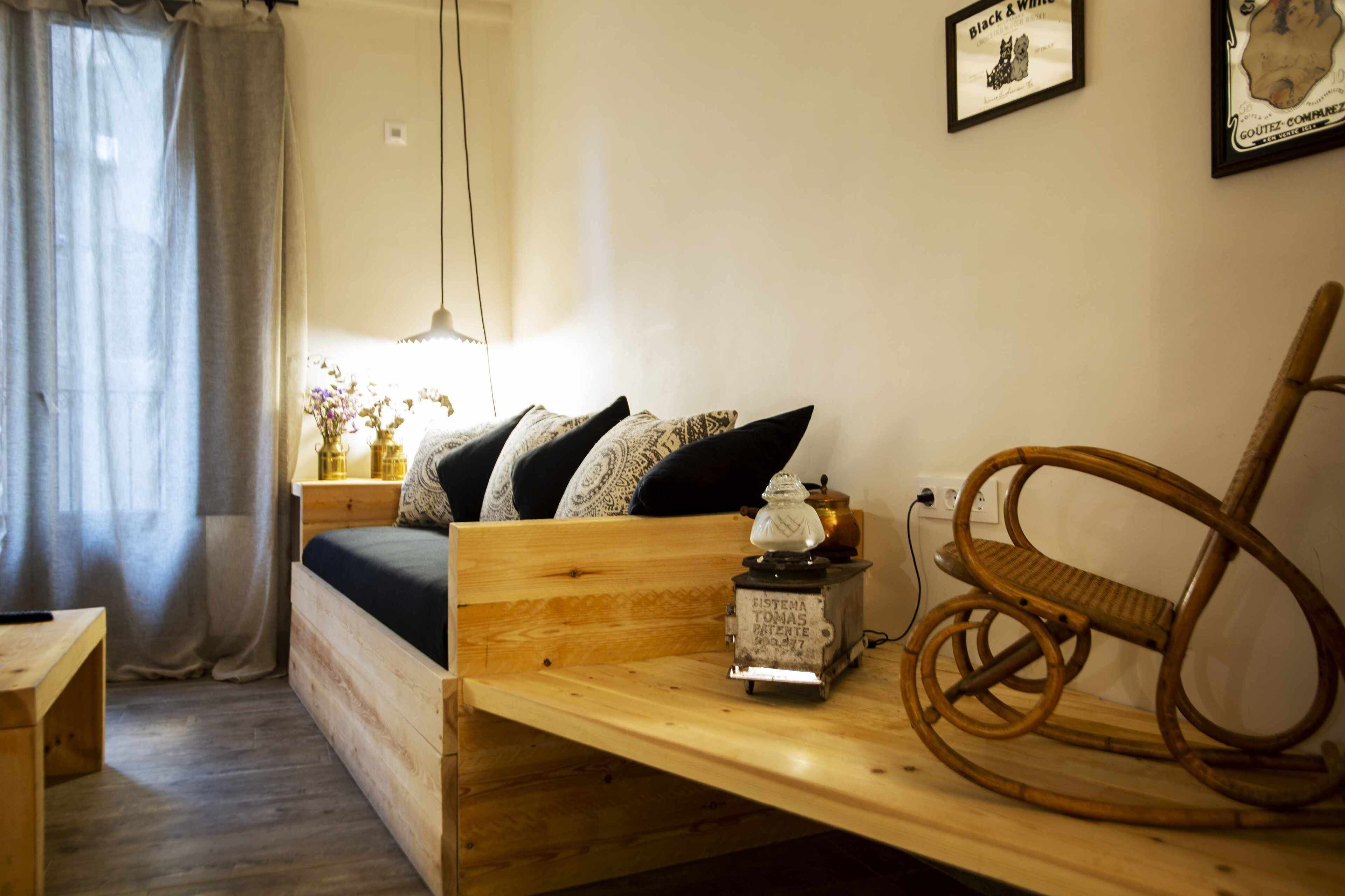 Une pièce chaleureuse avec un lit en bois, une petite table avec une lampe et un fauteuil en osier.