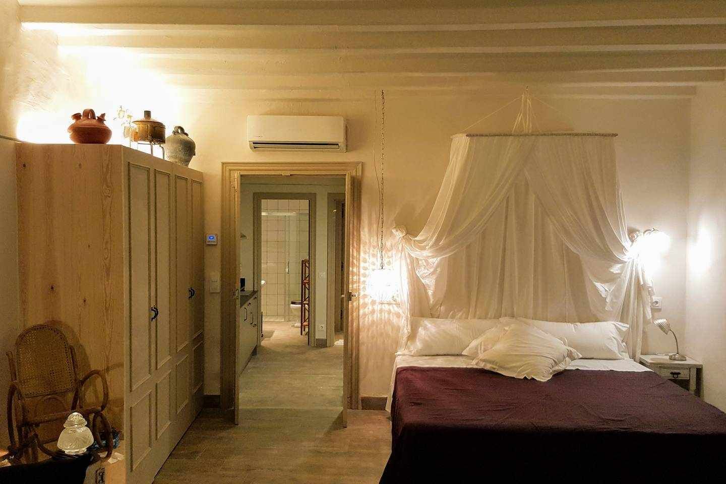 A bedroom with a canopy bed, wooden wardrobe, and a bathroom visible through an open door.