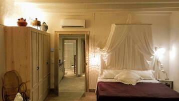 A bedroom with a canopy bed, wooden wardrobe, and a bathroom visible through an open door.