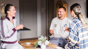 Un groupe de personnes est assis autour d’une table en bois, agrémentée d’un arrangement floral au centre, et elles sont engagées dans une conversation.