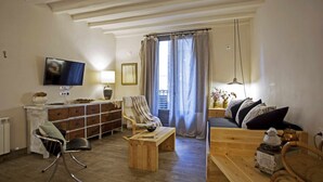 Un salon chaleureux avec une table basse en bois, un fauteuil confortable, un canapé, un téléviseur fixé au mur et une fenêtre avec des rideaux.