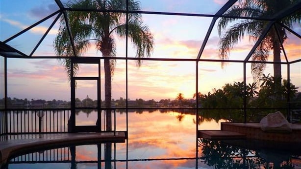 Una piscina con struttura in vetro, palme e vista sul tramonto.