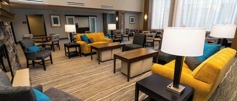 Un hall de hotel con arreglos de asientos, una chimenea y un ventanal con cortinas.