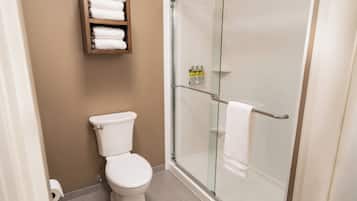 A bathroom with a toilet, a glass shower enclosure, and a shelf with towels.