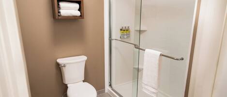 A bathroom with a toilet, a glass shower enclosure, and a shelf with towels.