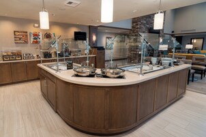 Un mostrador de buffet con diferentes estaciones de comida, una pared de piedra y un área de estar con un sofá y sillas.