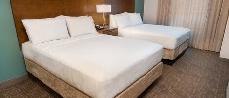 A hotel room with two beds, a nightstand with a lamp, and a large window with curtains.
