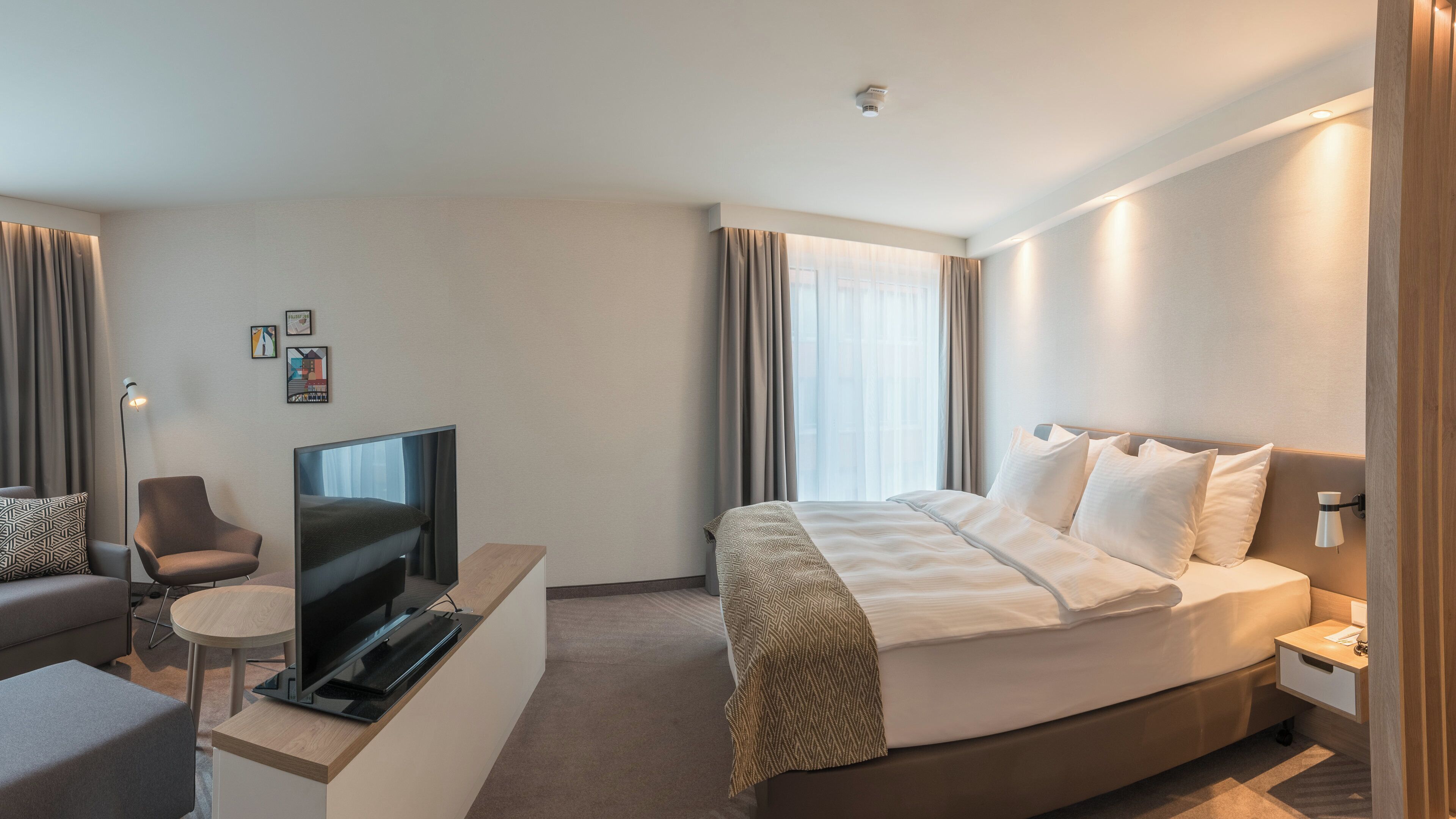 A hotel room with a bed, a TV, a desk, a chair, and a small table.