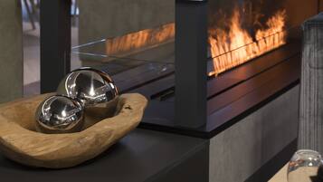 Un interior moderno con una chimenea de vidrio, un cuenco de madera con esferas metálicas y una mesa de vidrio.