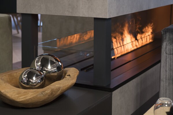 Un interior moderno con una chimenea de vidrio, un cuenco de madera con esferas metálicas y una mesa de vidrio.