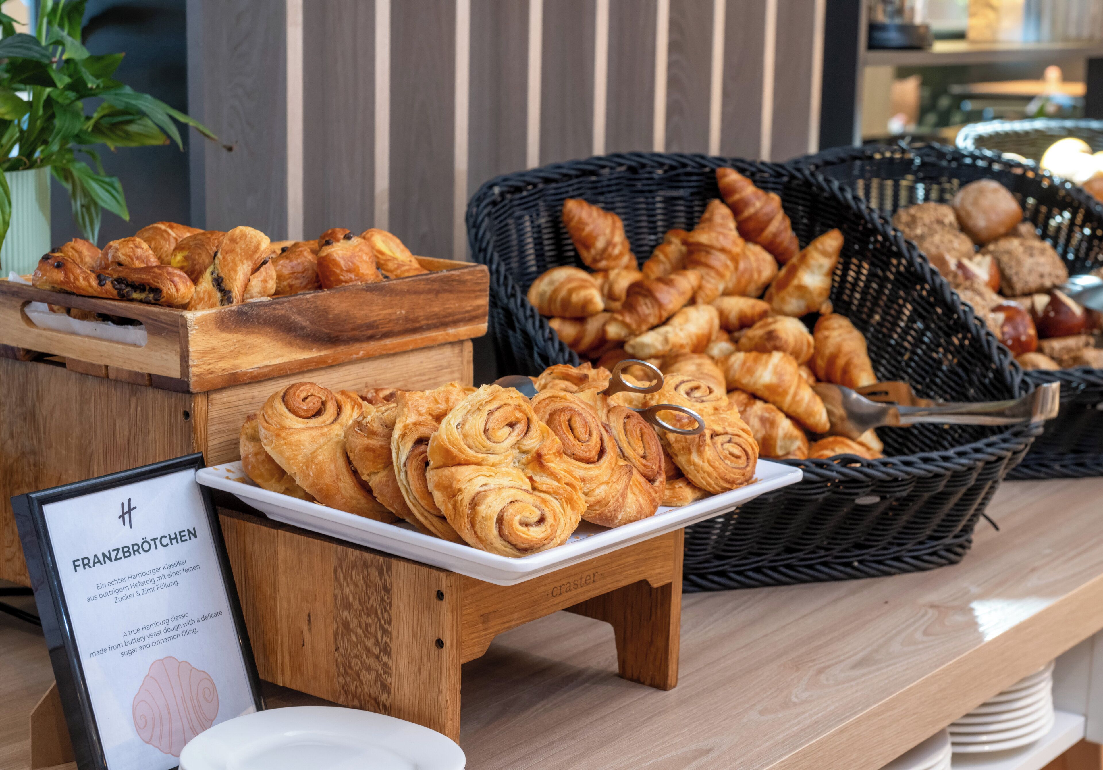 A display of various pastries and bread, including croissants and rolls, on a wooden table with a sign about Franzbröthchen.