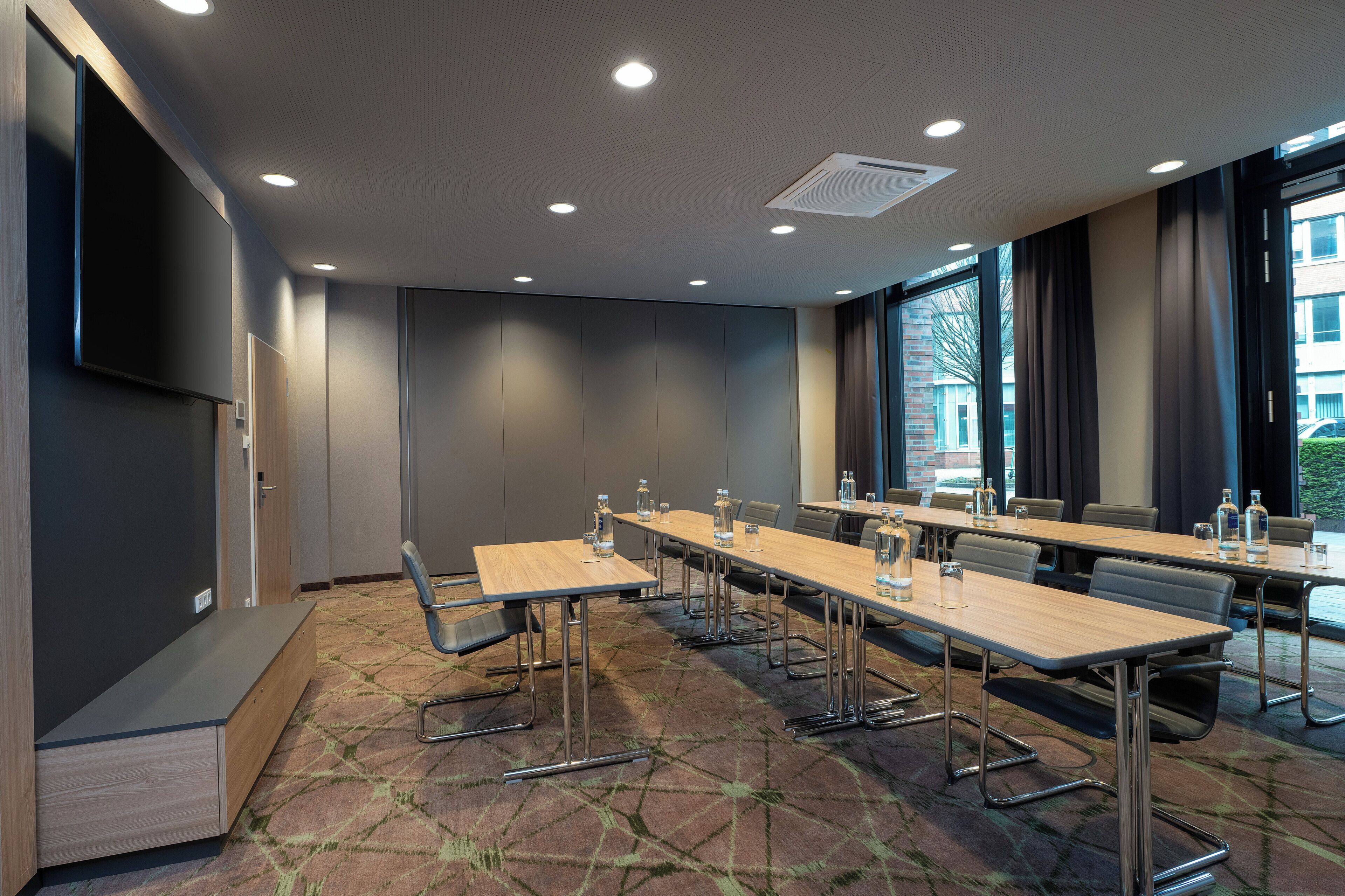Une salle de conférence équipée de longues tables, de chaises et d’un grand écran.