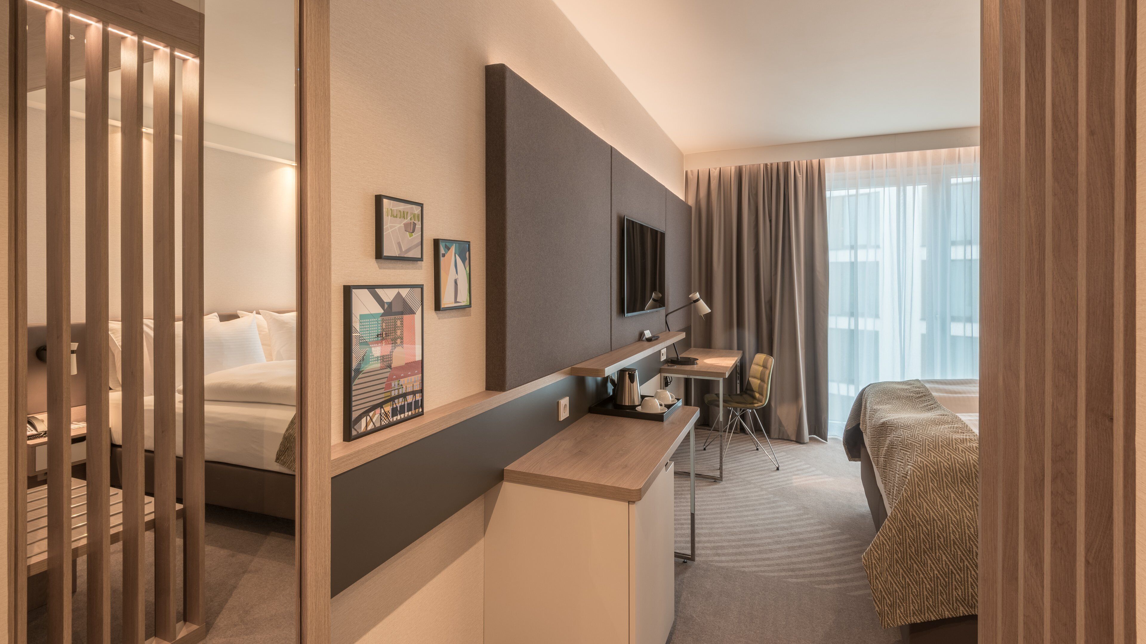 A hotel room with a bed, a desk, a chair, a TV, and artwork on the wall.