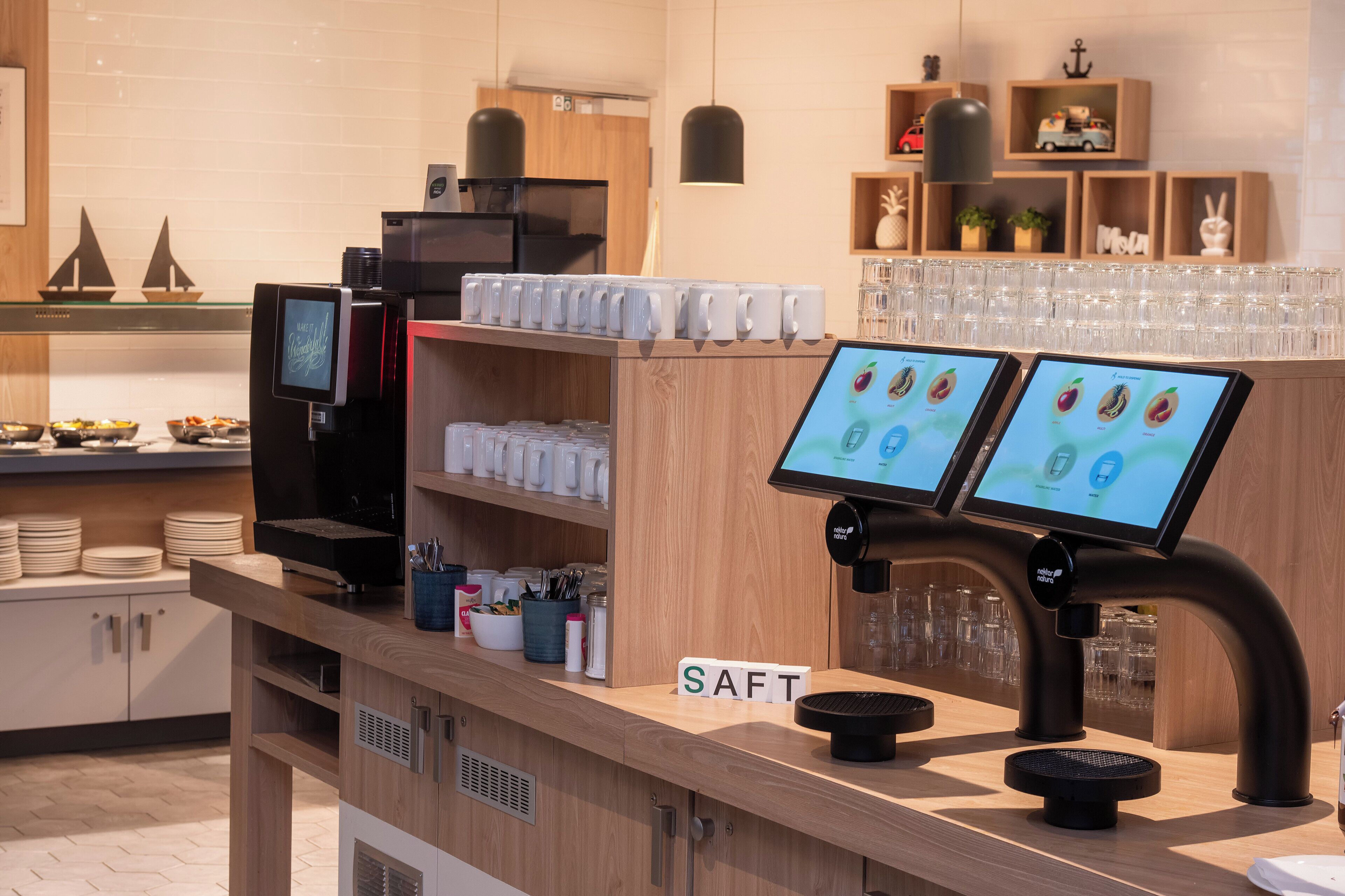 A modern coffee bar with digital menu screens, a coffee machine, and a 'SAFT' sign.
