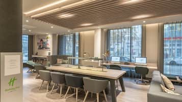 A modern hotel lobby with a long reception desk, comfortable seating, and large windows offering city views.