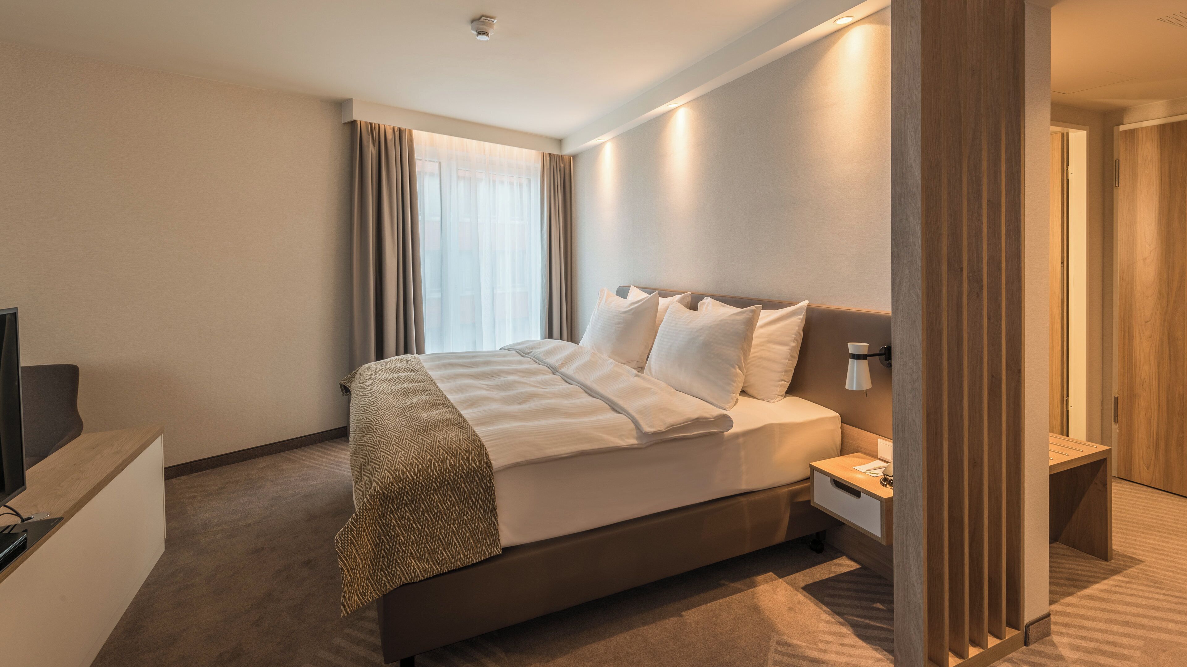 Ein Hotelzimmer mit Bett, Nachttisch, Lampe und Fernseher.