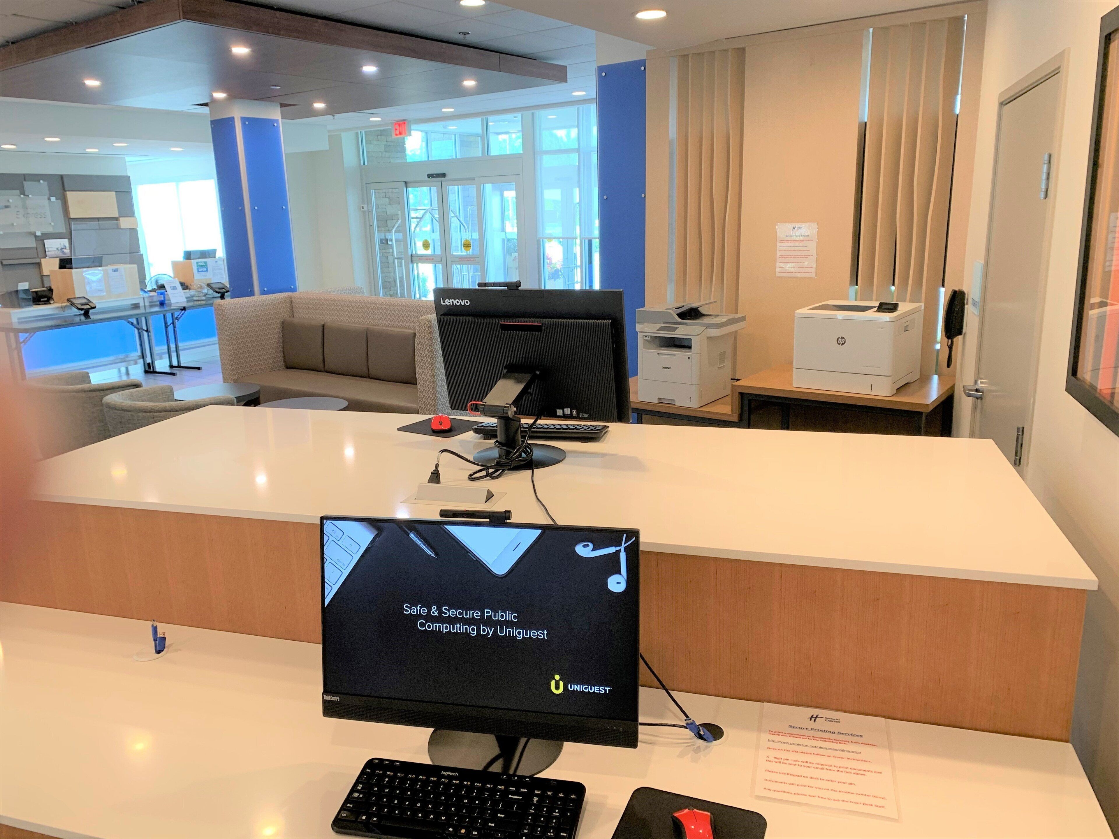 A reception desk with a computer monitor displaying a public computing service advertisement, a keyboard, a mouse, and a printer.
