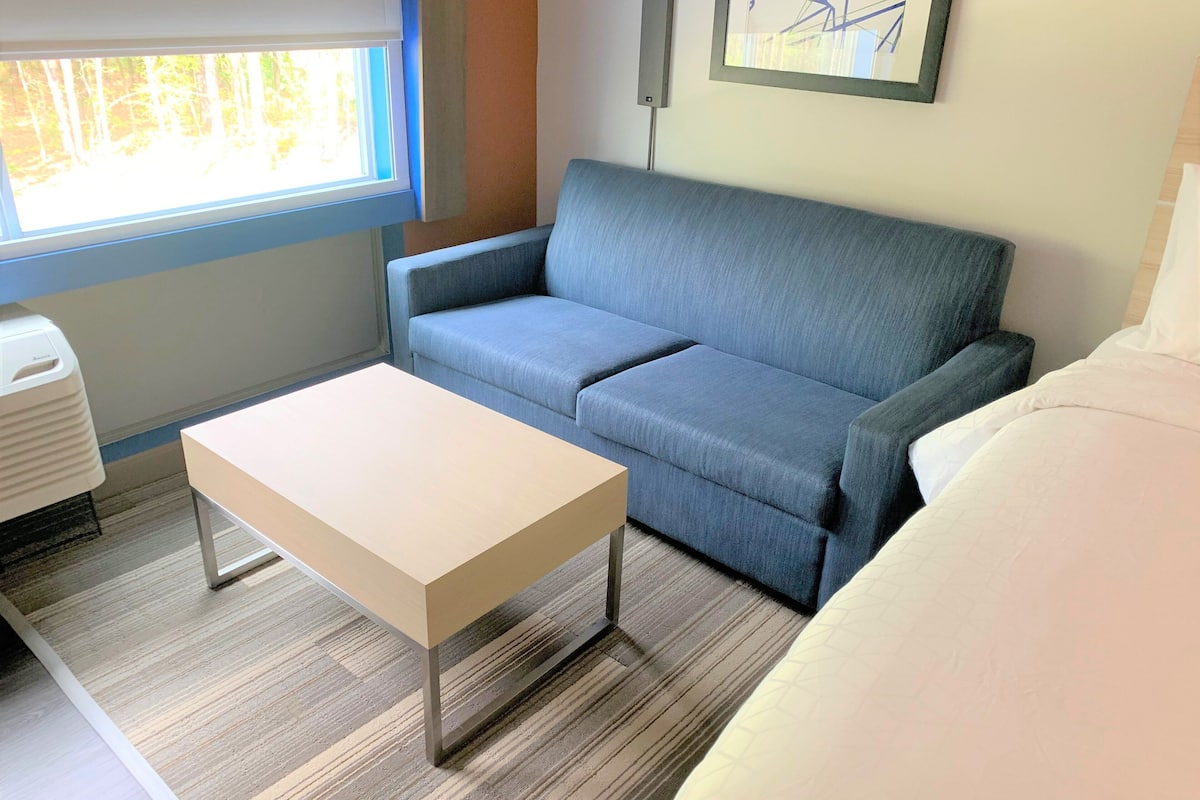 A room with a blue sofa, a white table, and a bed with white bedding.