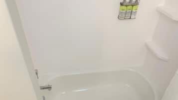 A bathroom with a white bathtub, a shower, and a toilet. There are three bottles of shampoo on the wall.