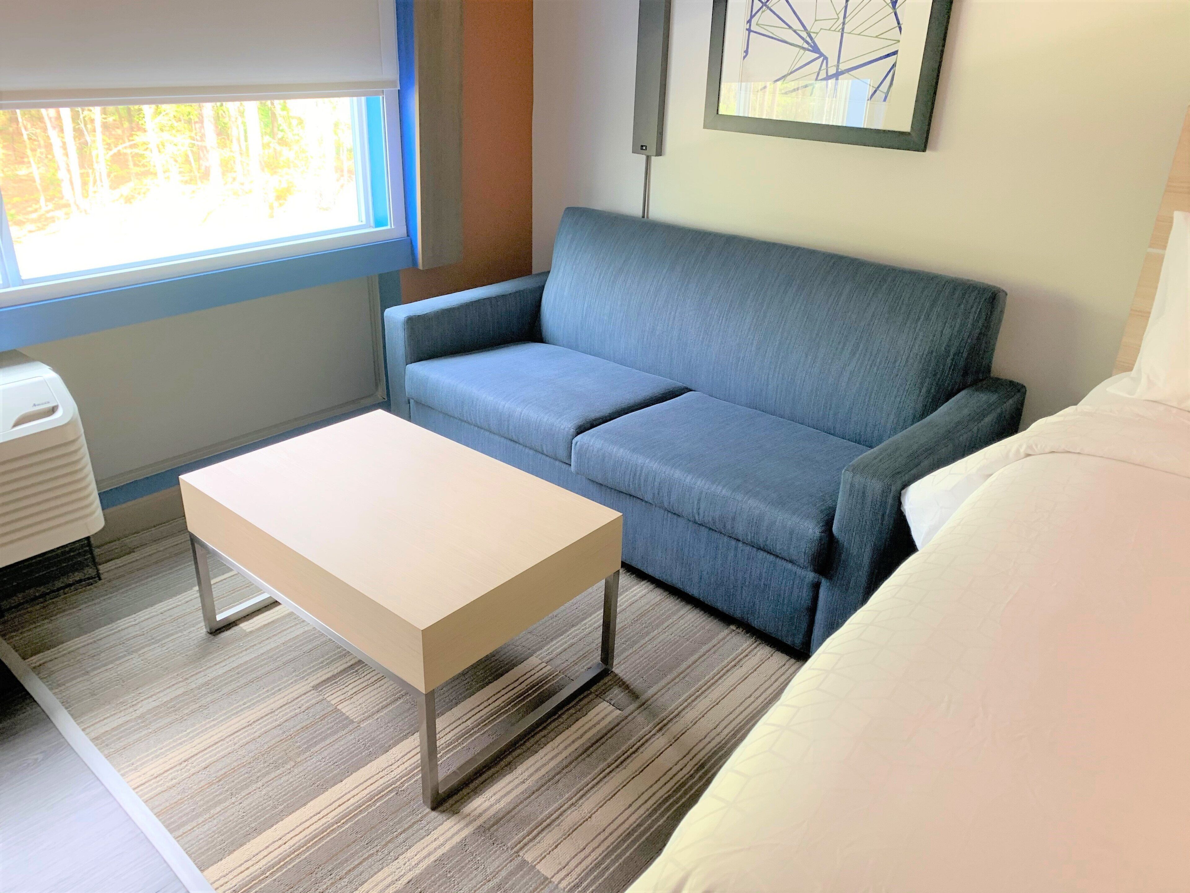 A room with a blue sofa, a white table, and a bed with white bedding.