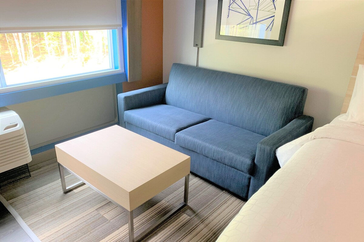 Una habitación con un sofá azul, una mesa blanca y una cama con ropa de cama blanca.
