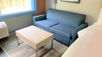 A room with a blue sofa, a white table, and a bed with white bedding.