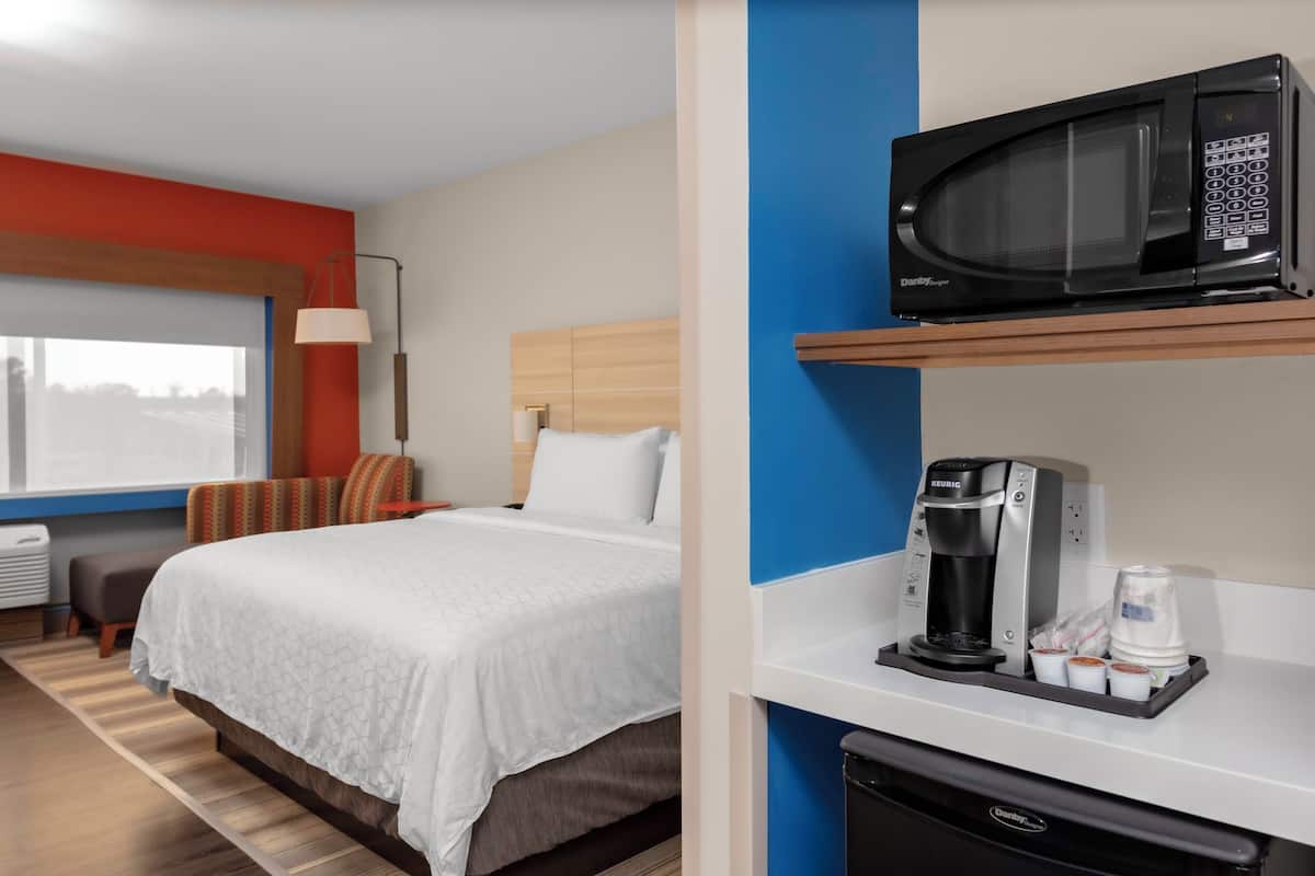 A hotel room with a bed, a microwave on a shelf, a coffee maker, and a window with a view.