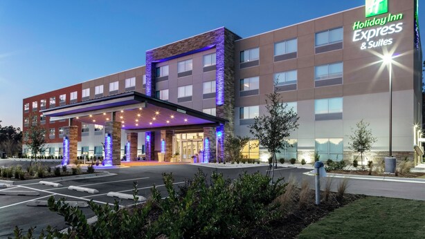 Edificio de Holiday Inn Express & Suites con diseño moderno, que presenta una entrada destacada con señalización iluminada y un corredor cubierto.