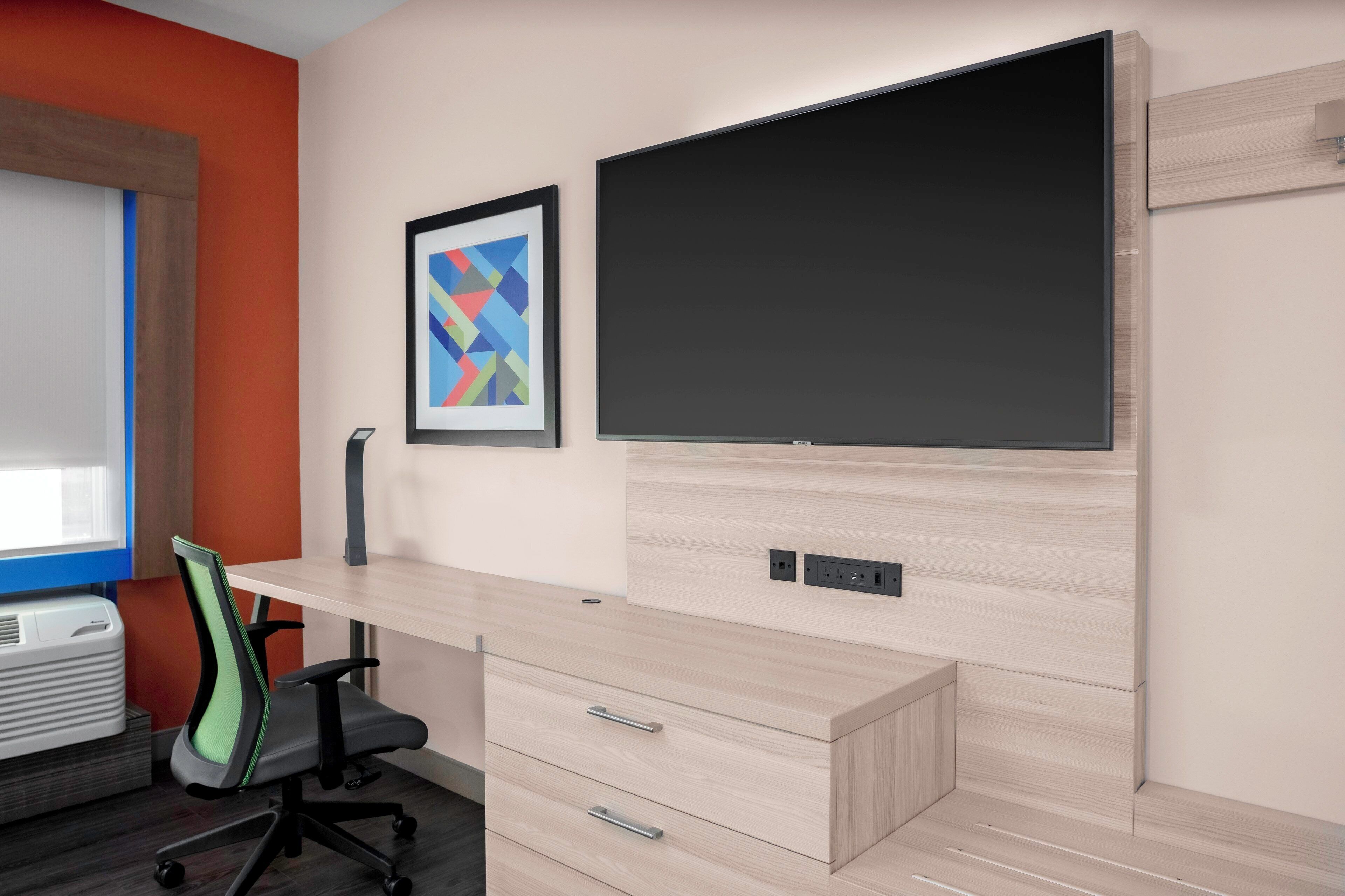 Un espacio de oficina moderno con un escritorio de madera clara, un monitor negro y una obra de arte abstracta enmarcada en la pared.