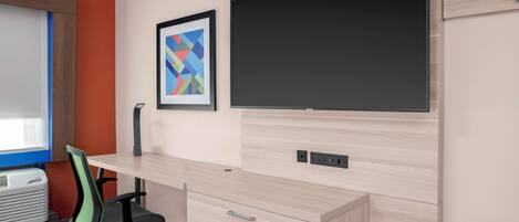 Un espacio de oficina moderno con un escritorio de madera clara, un monitor negro y una obra de arte abstracta enmarcada en la pared.