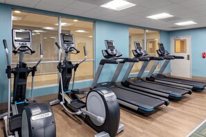 Une salle de remise en forme équipée de tapis de course et de vélos elliptiques, dotée de grandes fenêtres et d’une porte.