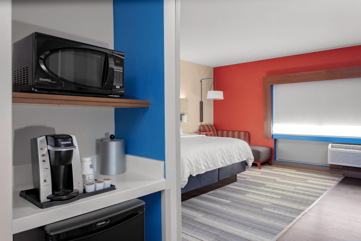 Una habitación de hotel con cama, cafetera, microondas y un ventanal grande.
