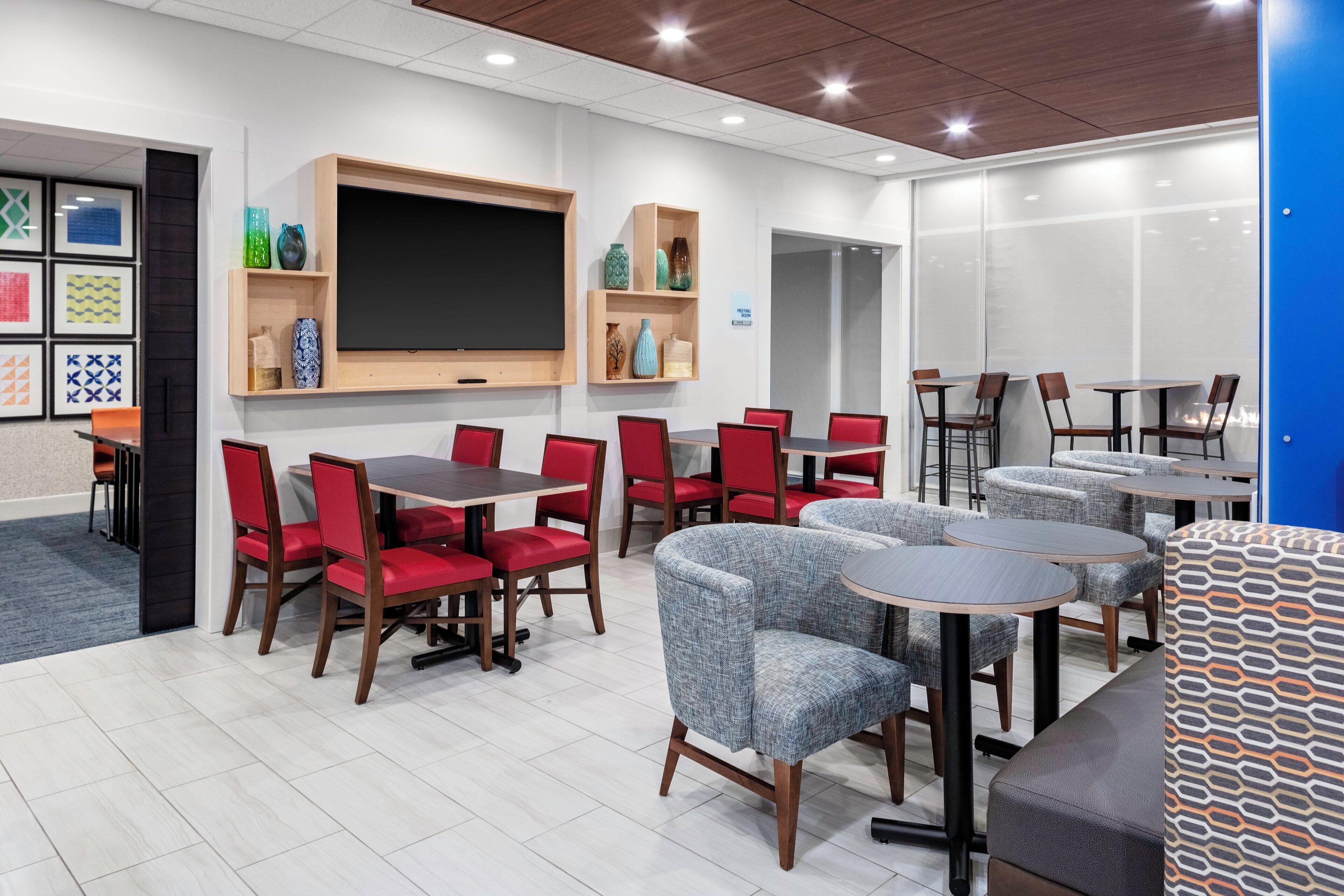 A meeting room with a large screen, red and grey chairs, and a blue wall.