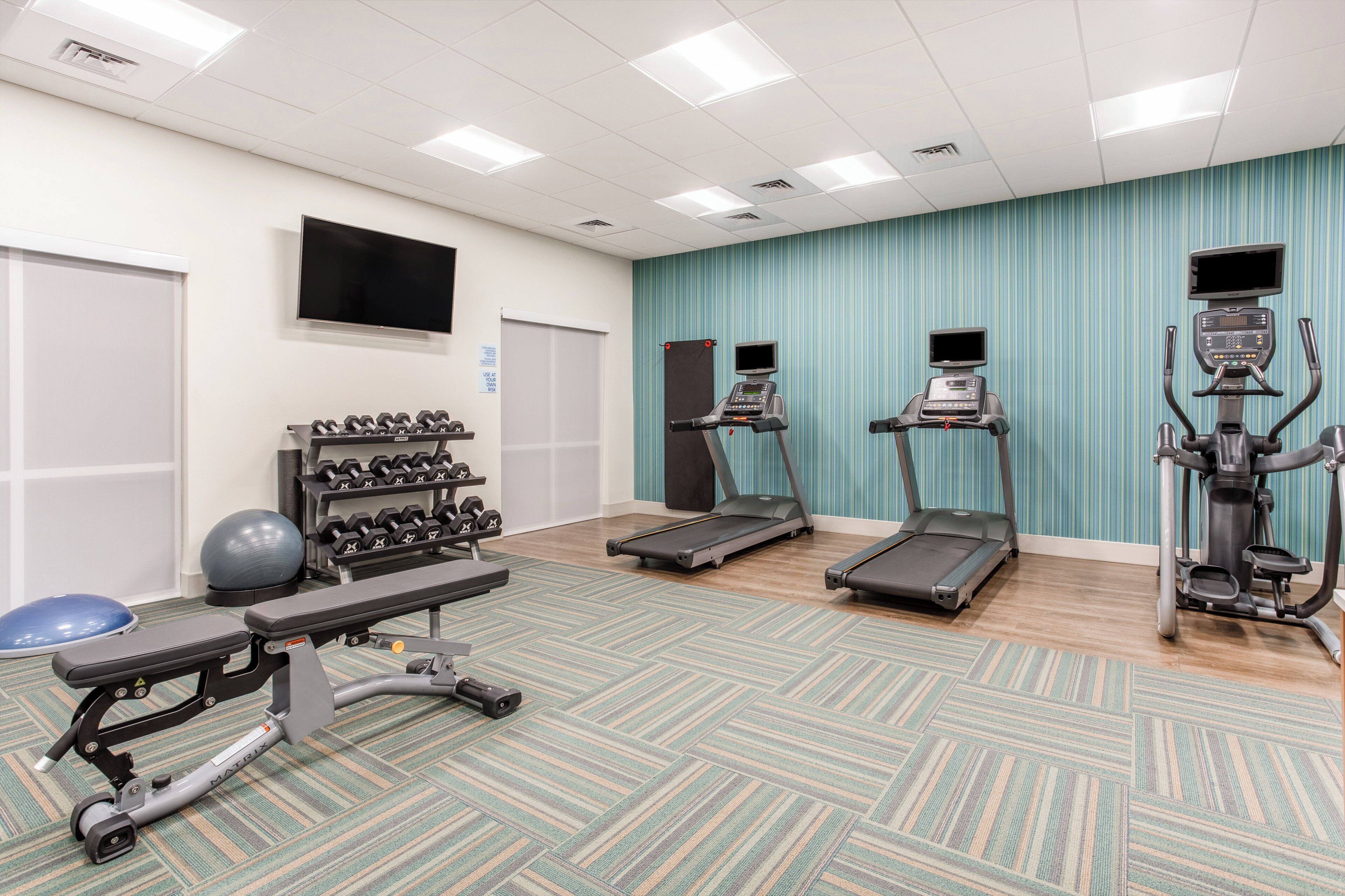 Un gimnasio con cintas de correr, elípticas, una prensa de banca, mancuernas y una bicicleta estática.