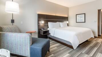 A hotel room with a large bed, a desk with a chair, a sofa, and a lamp.