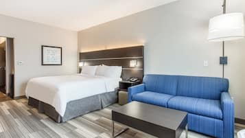 A hotel room with a bed, a sofa, a nightstand, a lamp, and a framed picture on the wall.