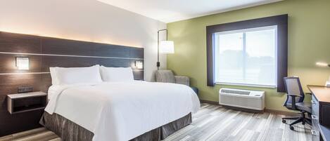 A hotel room with a bed, bedside table, lamp, desk, chair, and a large window.
