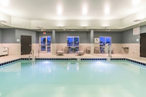 A swimming pool with chairs and a pool lift, surrounded by walls with windows.