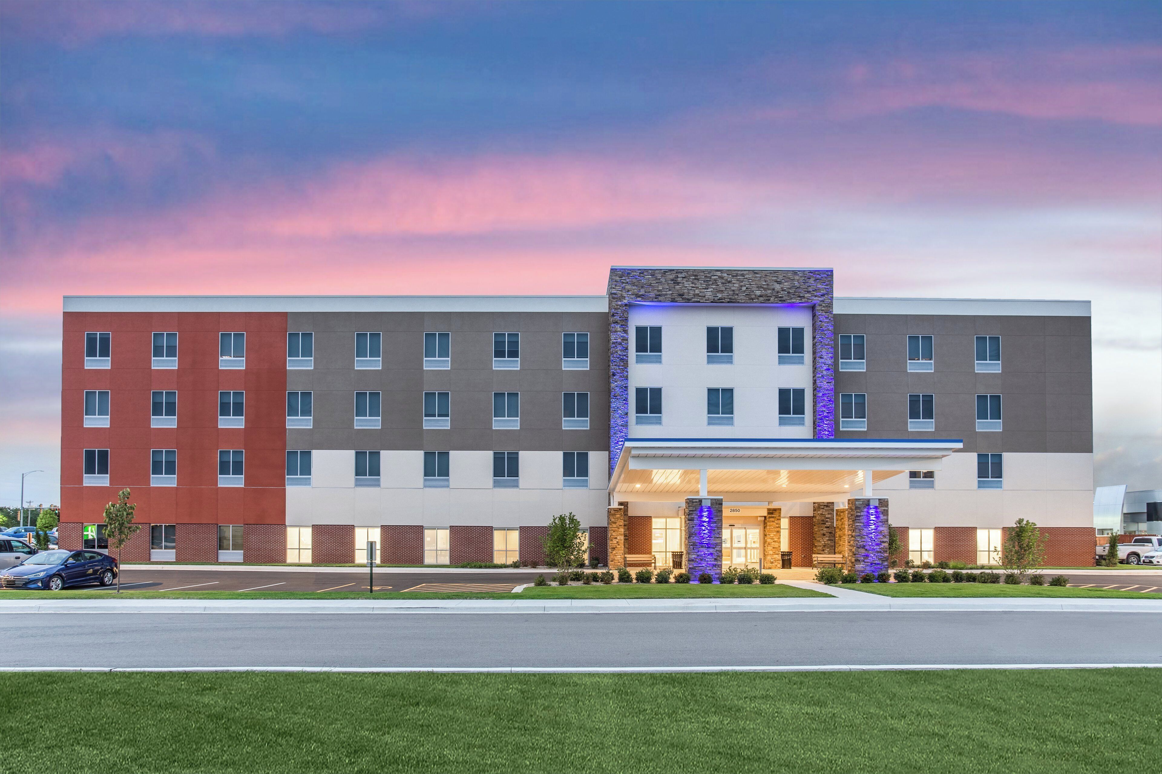 A multi-story hotel with a flat facade, a central entrance with a covered walkway, and a parking lot in front.