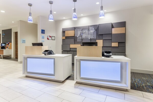 A hotel reception area with two reception desks, overhead lighting, and a wall-mounted sign.